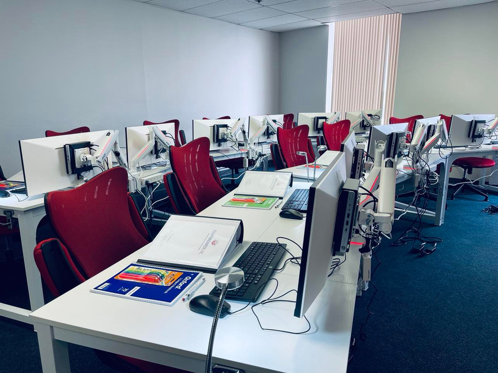 A reverse view across Flight Innovation classroom desks, monitor arms, and reference books.